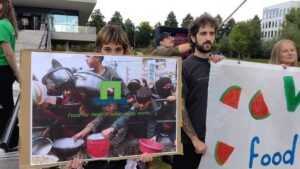 Een demonstrant laat een protestbord zien van Palestijnse mensen die gretig hun pannen naar voren houden, met over de foto heen het logo en de slogan van de WUR: "Food for health: what really works."